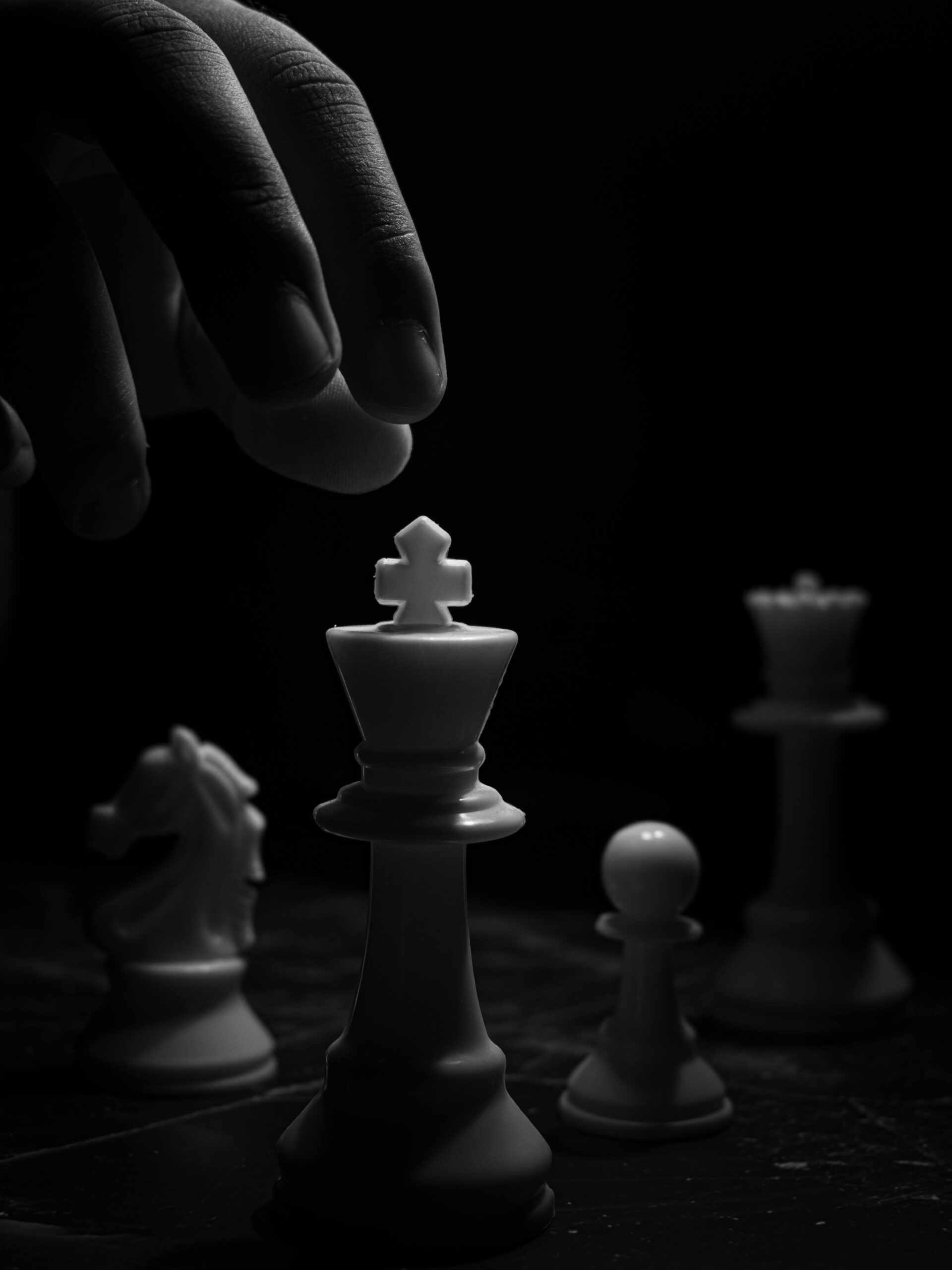 A dramatic black and white photo of chess pieces under dim light, showcasing strategy and focus.